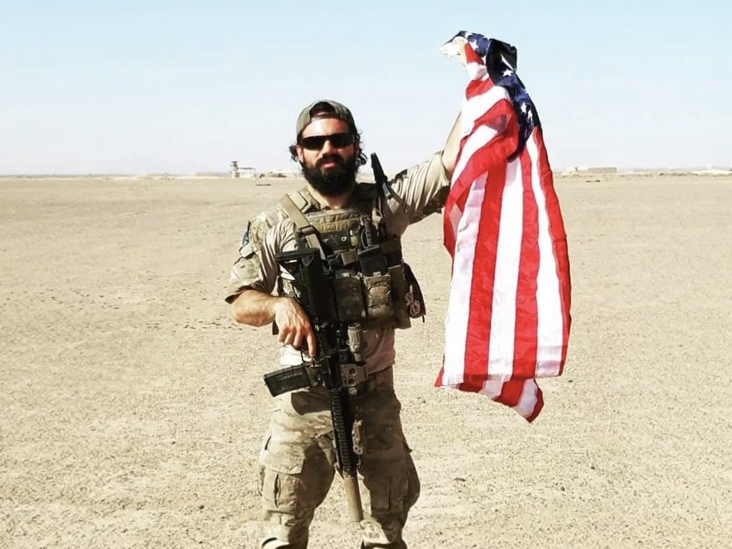 Staff Sergeant Cole Condiff in uniform, holding an American flag